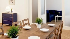A dining area with a long wooden table set for six, surrounded by wooden chairs. There are potted plants on the table, and a dark blue sofa is visible in the background. - Prague Central Residence (Prague)