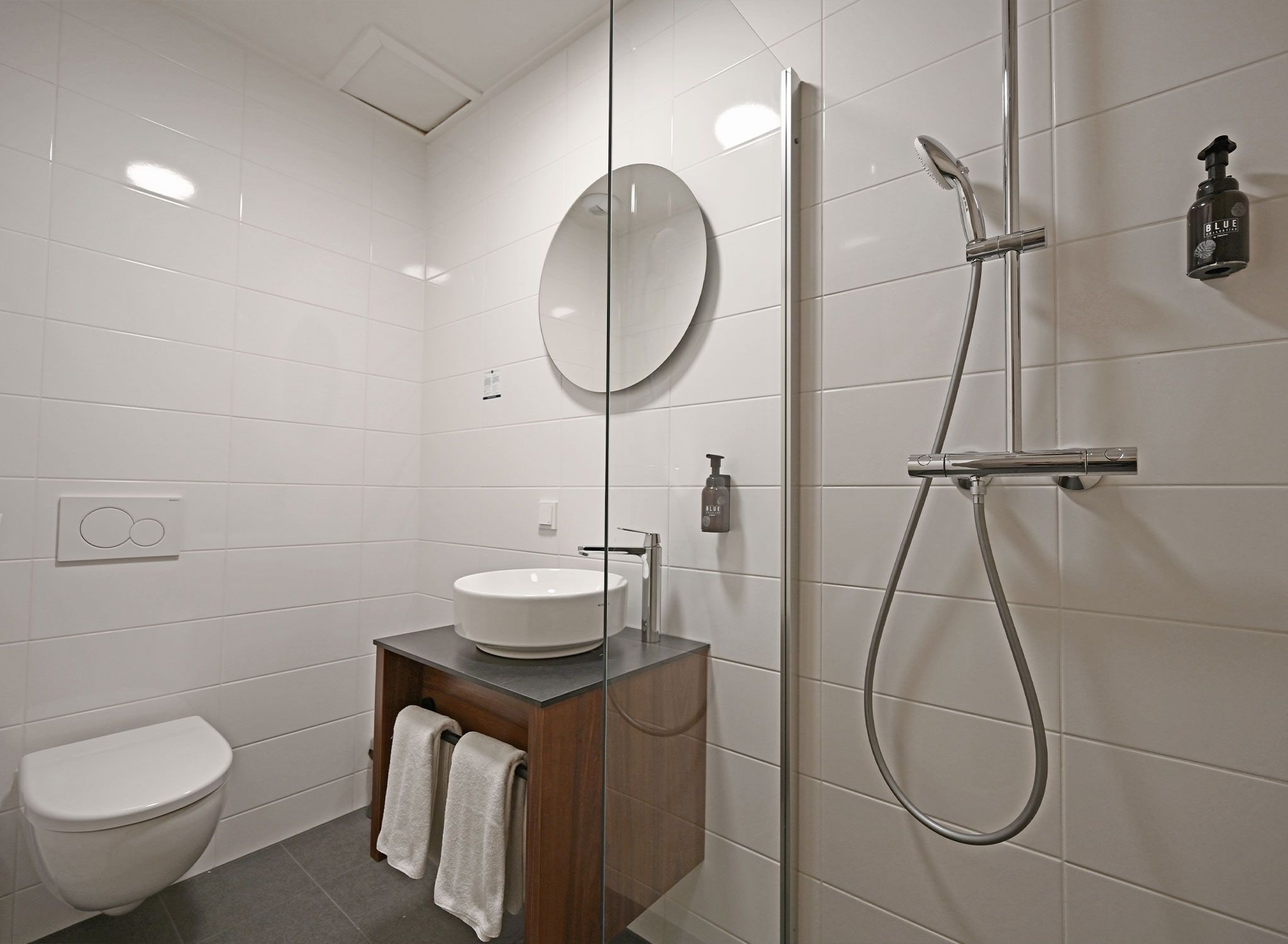 Un baño moderno con ducha envuelta en vidrio, un lavamanos blanco y un mueble de tocador de madera.