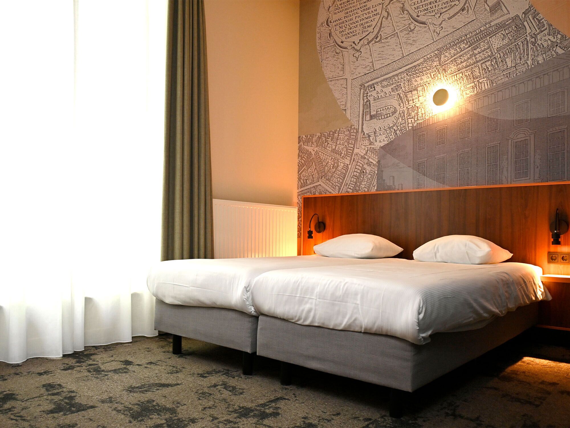 A hotel room with a double bed, a headboard with a map, a wall-mounted light, and a window with curtains.