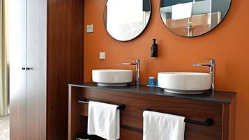 A bathroom with two sinks, a mirror, a towel rack, and a trash can.