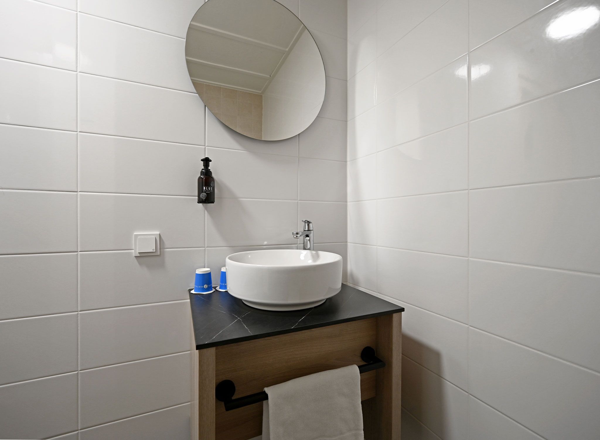 A bathroom with a white sink, a round mirror, a towel rack, and a bottle of soap.