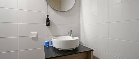 A bathroom with a white sink, a round mirror, a towel rack, and a bottle of soap.