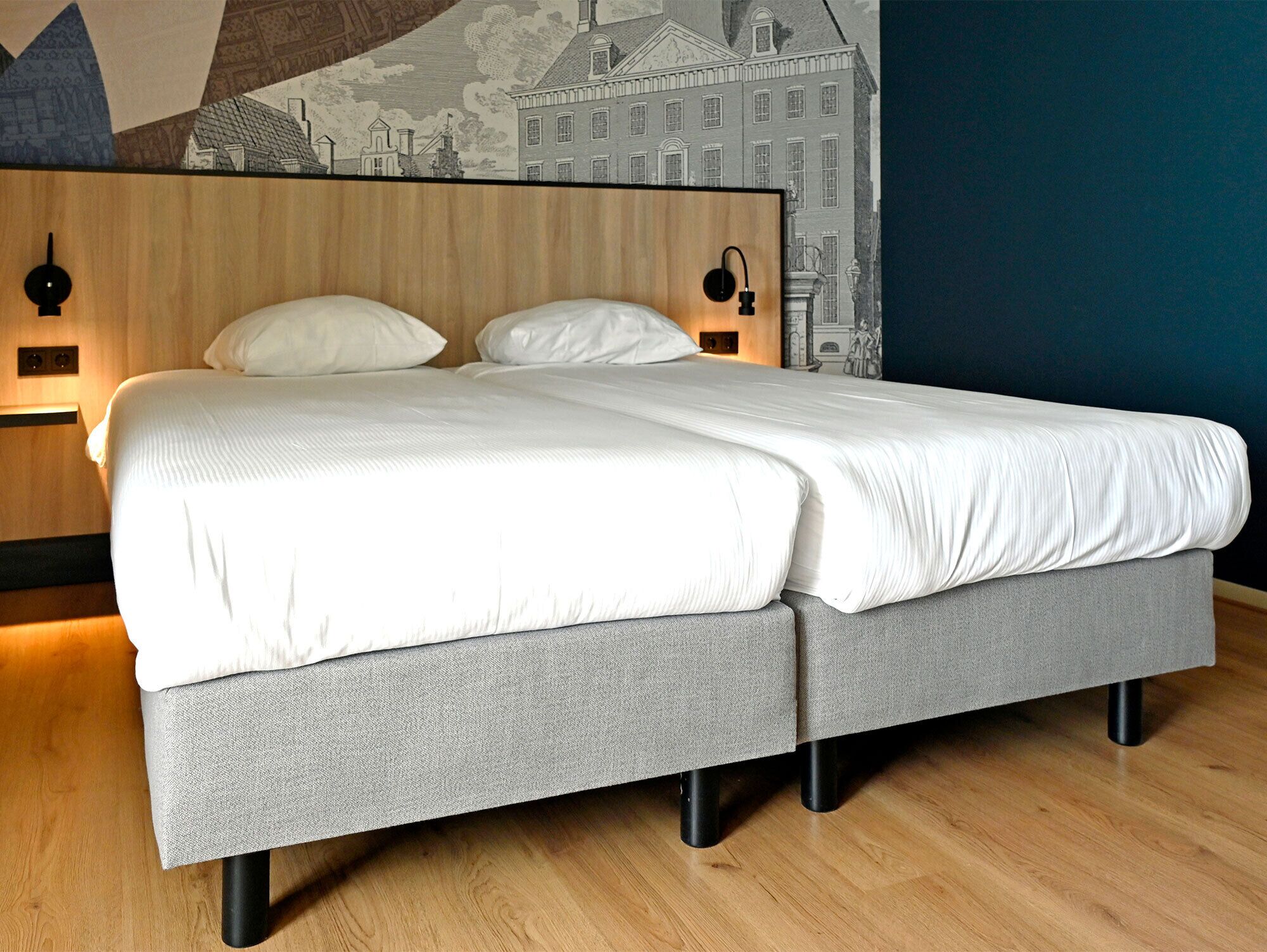 A double bed with a grey upholstered base, a wooden headboard, and two bedside lamps.