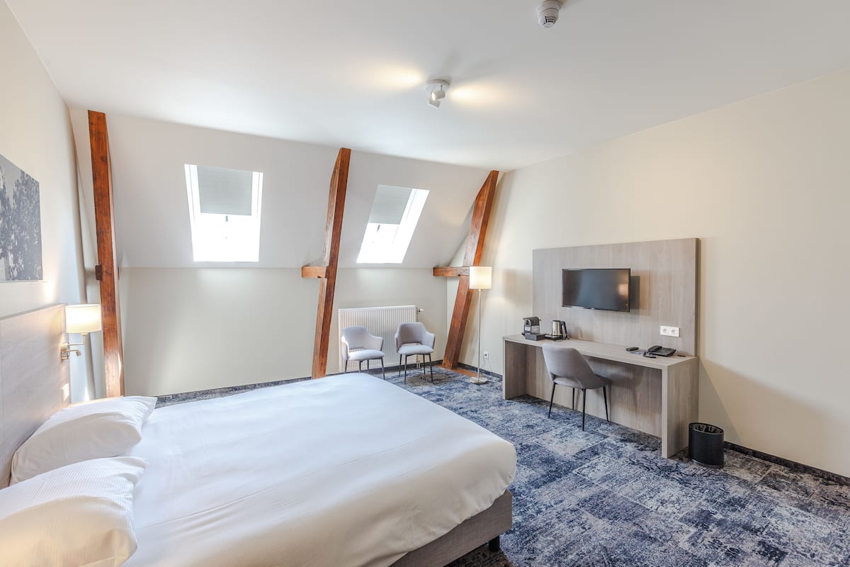 Une chambre d’hôtel avec un lit, deux chaises, un bureau avec un ordinateur, une télévision et une fenêtre.