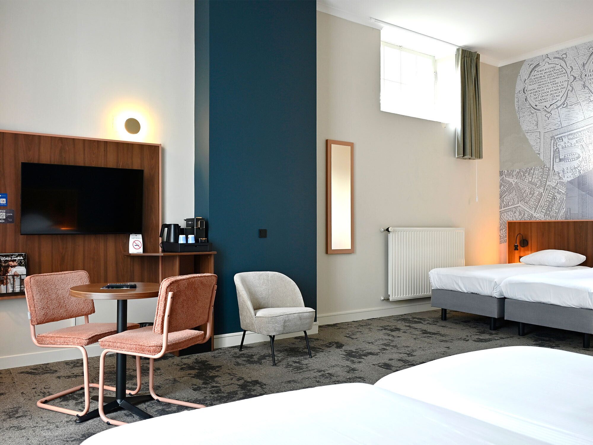 Ein Hotelzimmer mit Fernseher, einer Kaffeestation, zwei Sesseln, einem Bett und einer Karte an der Wand.
