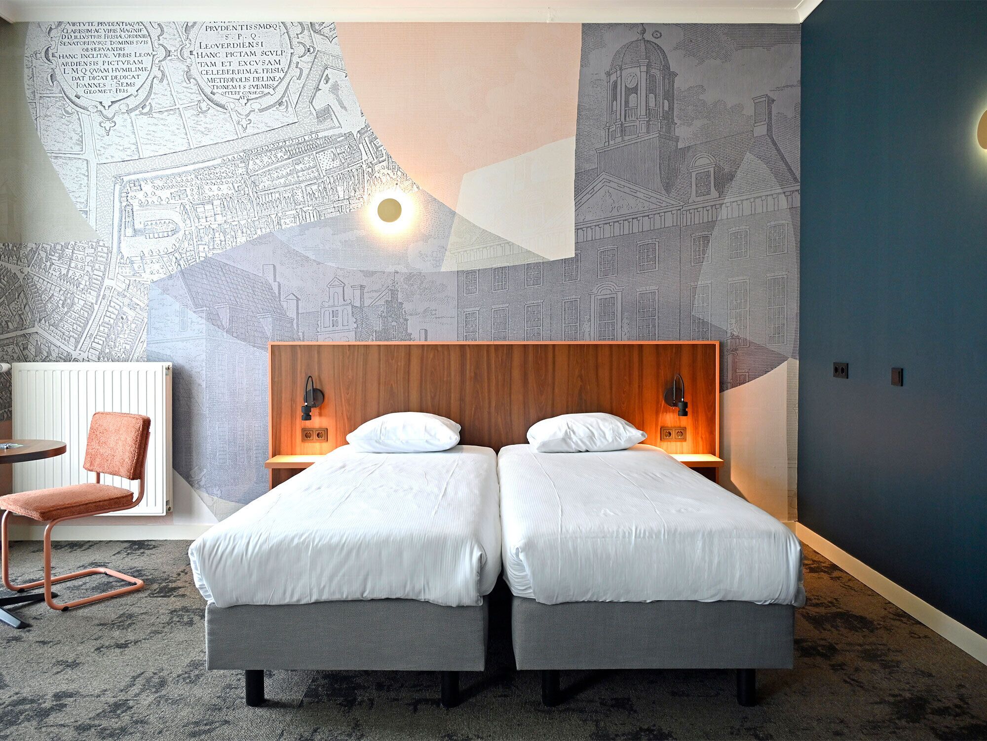 A hotel room with two beds, a wooden headboard, a map mural, a chair, and a desk.