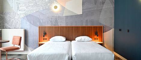 A hotel room with two beds, a wooden headboard, a map mural, a chair, and a desk.