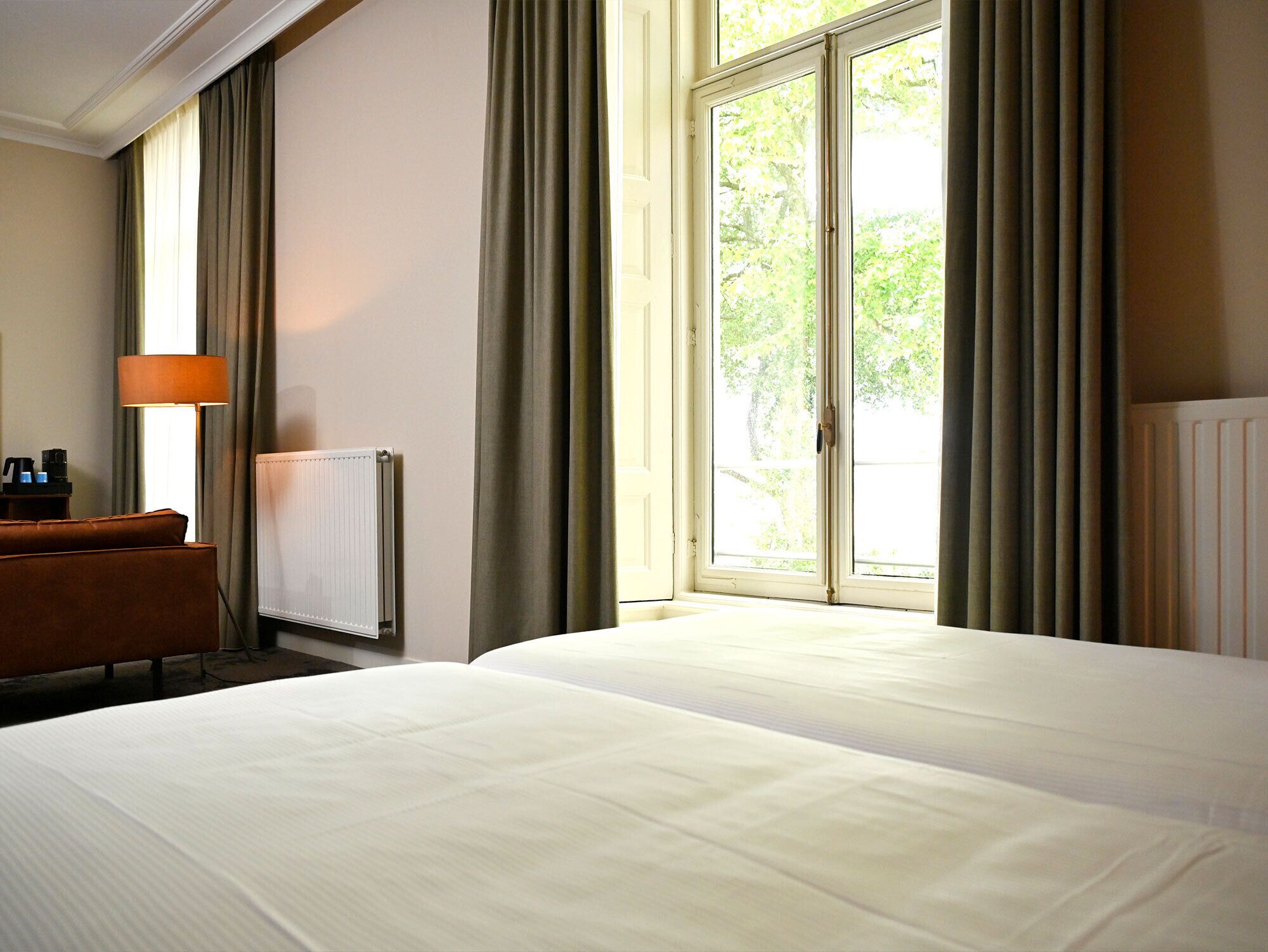 A hotel room with a bed, a desk, a lamp, and a window with curtains.