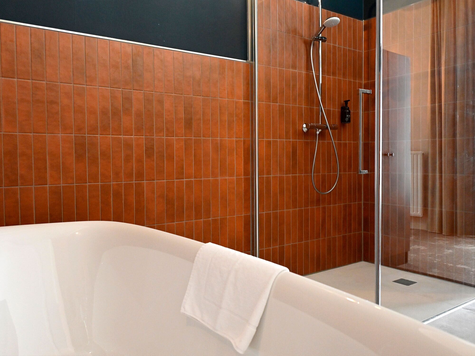 A modern bathroom with a glass-enclosed shower, a white bathtub, and a tiled wall.