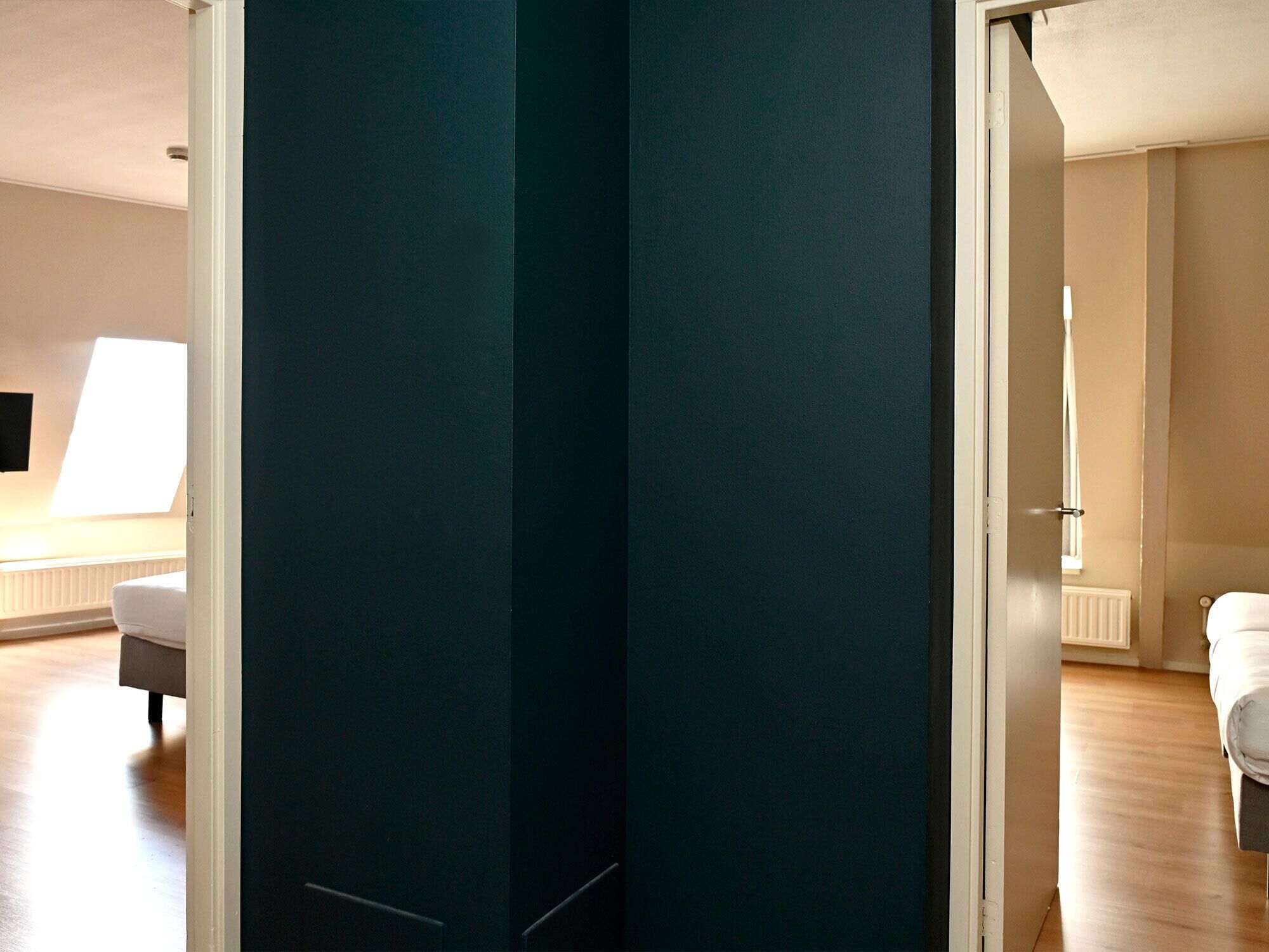 A room with a dark-colored door, a white radiator, a white sofa, and a white chair.