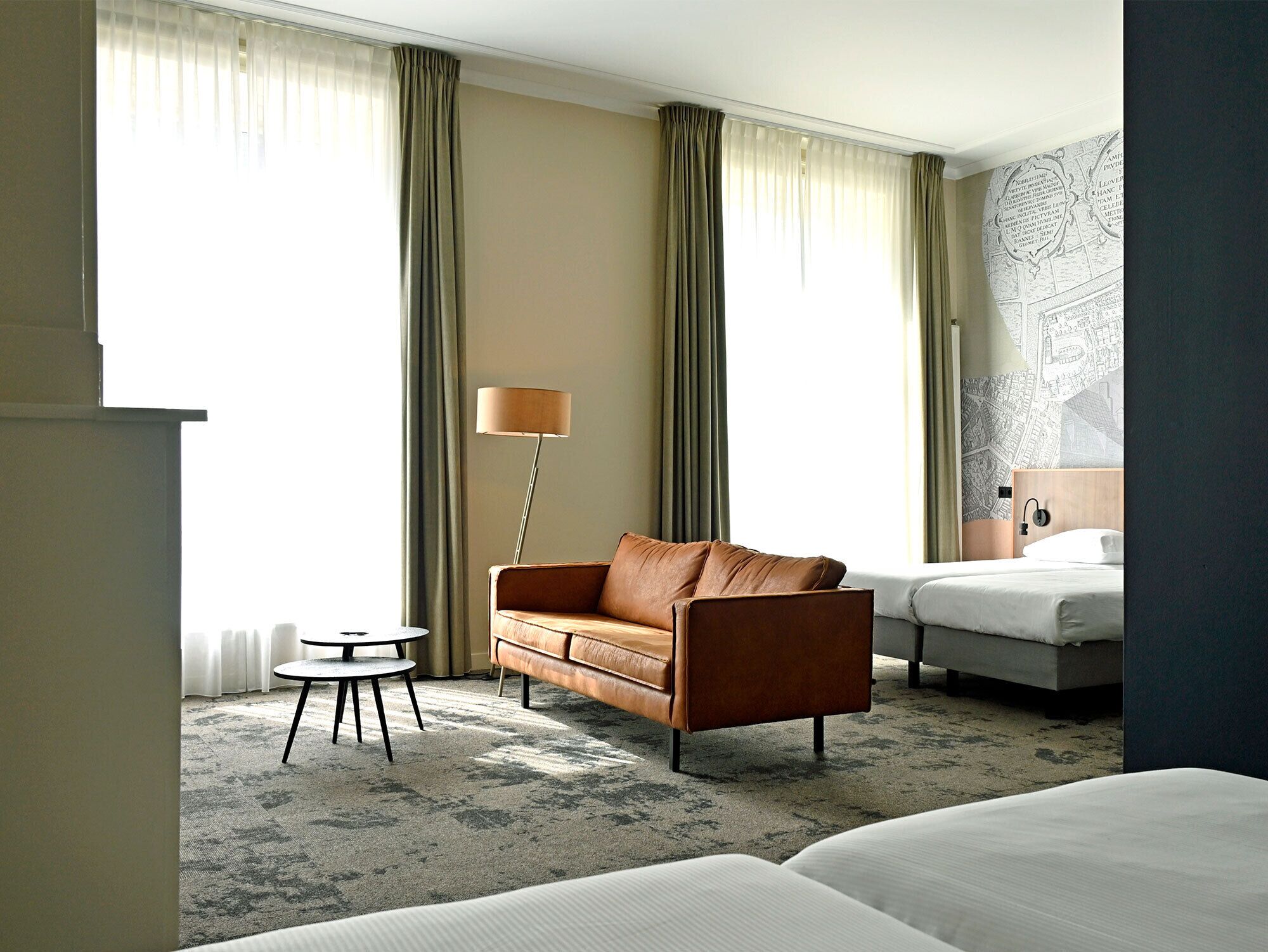Une chambre d’hôtel avec un canapé, une petite table ronde, une lampe, un lit et une carte accrochée au mur.