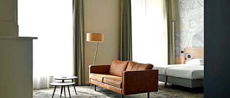 Une chambre d’hôtel avec un canapé, une petite table ronde, une lampe, un lit et une carte accrochée au mur.