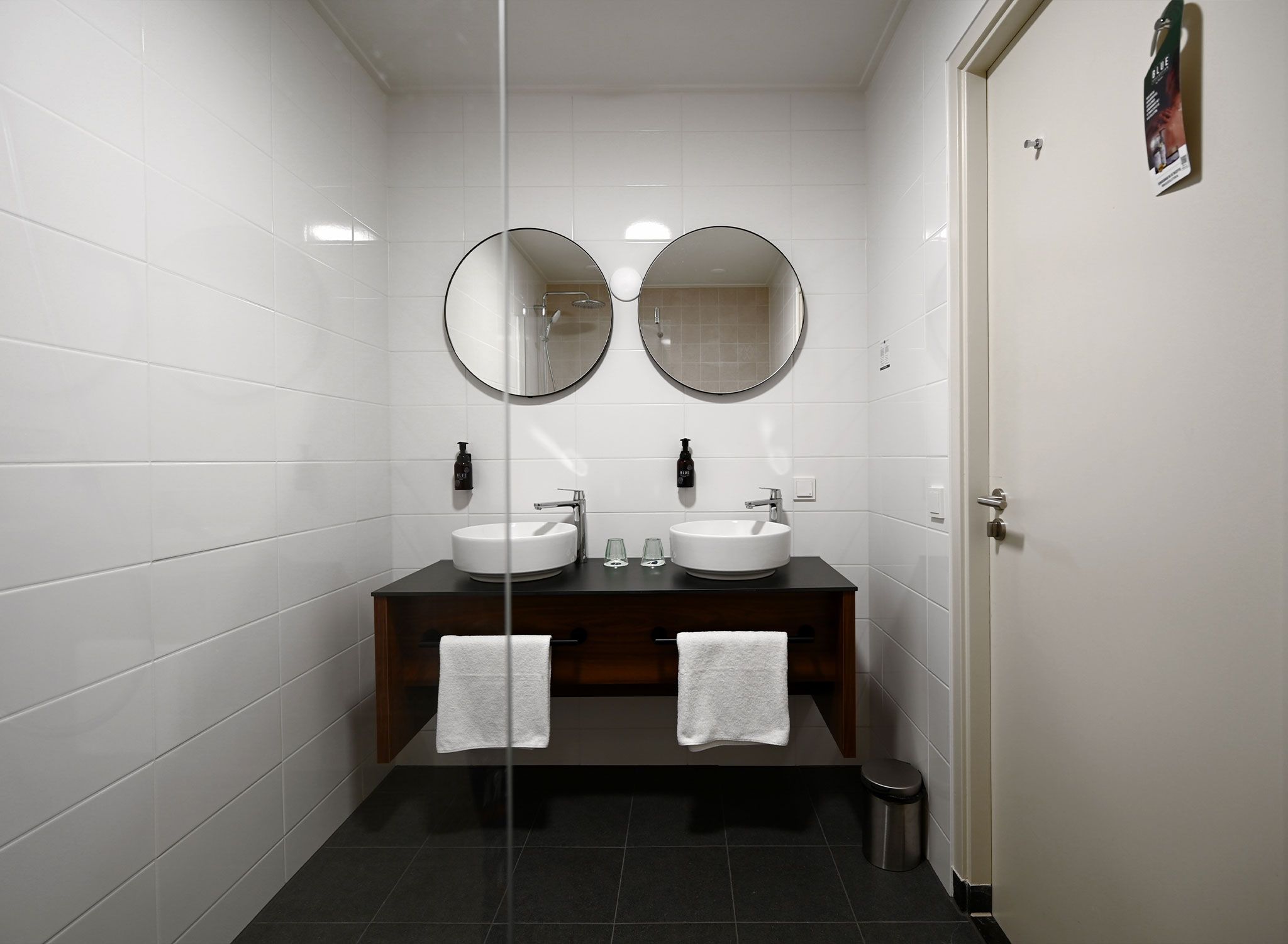 A modern bathroom with two sinks, a dark wooden vanity, and a glass partition.