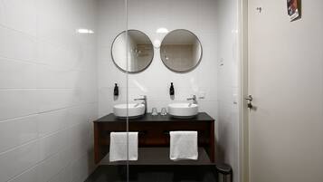 A modern bathroom with two sinks, a dark wooden vanity, and a glass partition.