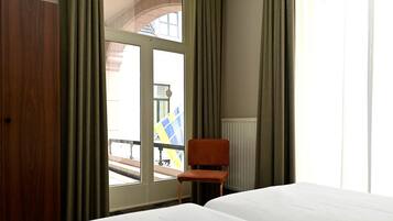 Une chambre d’hôtel avec un lit, une chaise, une fenêtre avec des rideaux et une vue sur l’extérieur.
