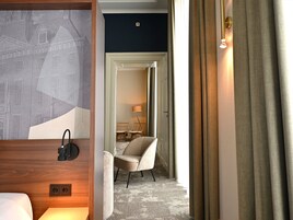 Habitación de hotel con cama, una silla, una lámpara y vista a otra habitación.