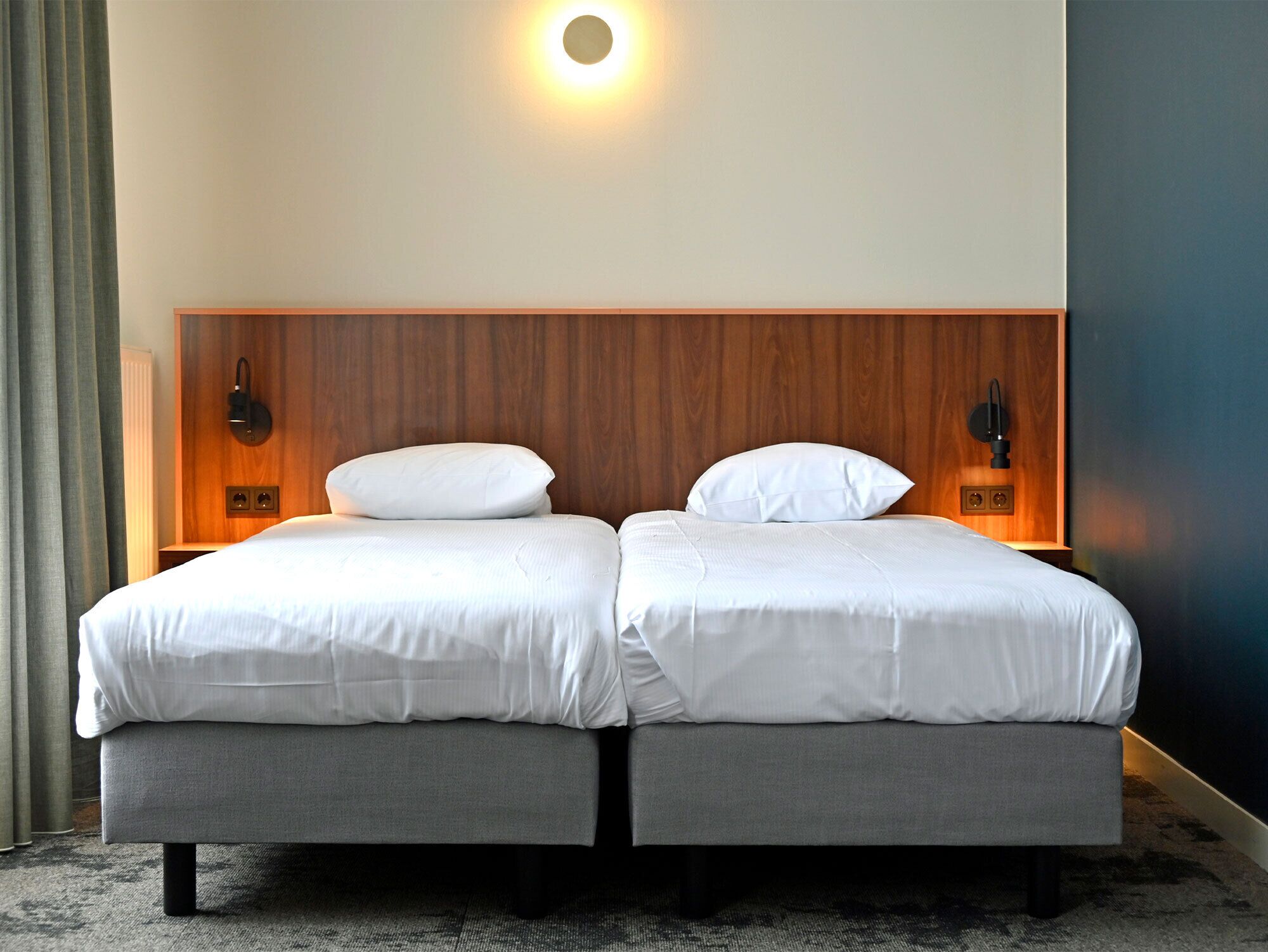 Una cama doble con cabecera de madera, dos lámparas de noche y una pared de color neutro.
