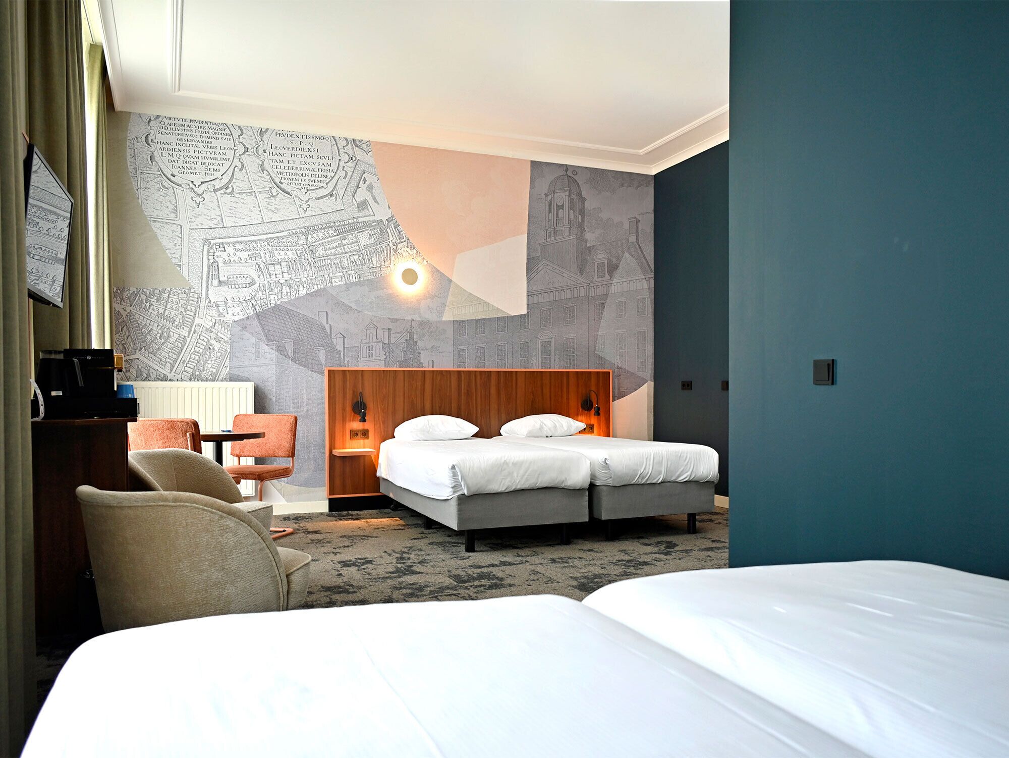 Ein Hotelzimmer mit einem großen Bett, einem Schreibtisch mit Stuhl, einer Wand mit einer Karten-Grafik und einem Nachttisch mit Lampe.
