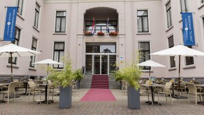 Una entrada de hotel con alfombra roja, asientos exteriores con sombrillas y plantas en macetas.
