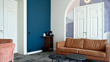 A room with a blue wall, a brown leather sofa, two small round tables, and a door with a white frame.