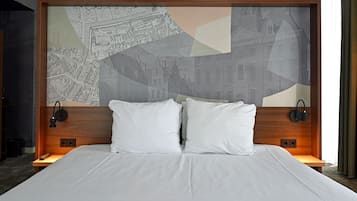 Una camera d'albergo con un letto grande, due cuscini, una testiera con motivo urbano e lampade ai comodini.
