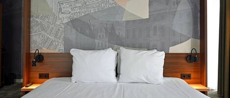 Habitación de hotel con una cama grande, dos almohadas, un cabecero con diseño de paisaje urbano y lámparas de noche.