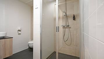 A modern bathroom with a glass-enclosed shower, a toilet, and a sink with a wooden countertop.