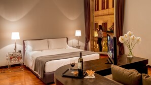 A hotel room with a bed, bedside lamps, a TV, a dining table with a bottle of wine, and a vase with flowers. - Suitedreams (Rome)