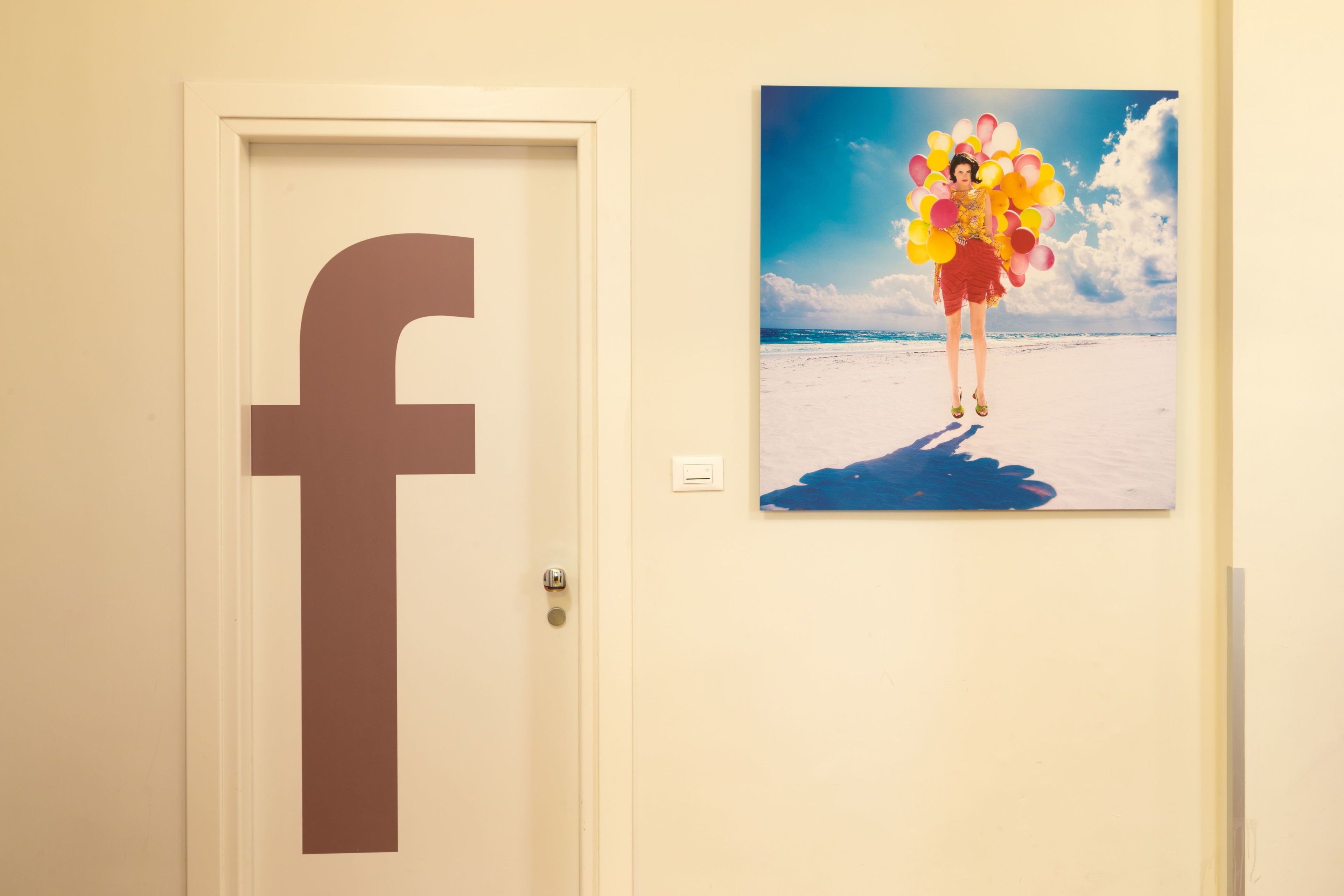 A door with a large Facebook logo and a painting of a person holding balloons on a beach.
