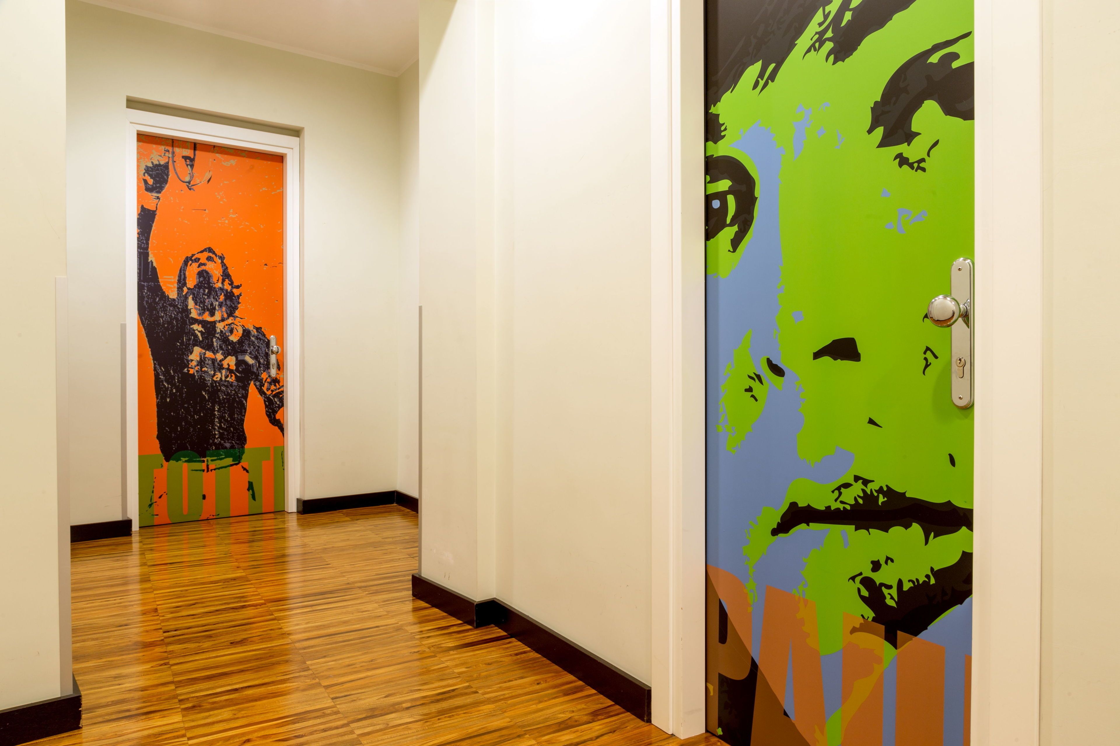 A hallway with wooden flooring, a door with a colorful mural, and a white wall.