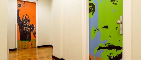 A hallway with wooden flooring, a door with a colorful mural, and a white wall.
