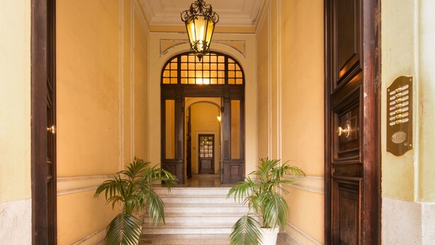 A grand entrance with a marble staircase, a large arched doorway, and two potted plants. - Suitedreams (Rome)