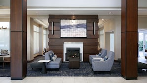 A modern lobby with a fireplace, two sofas, and a coffee table. - Hilton Garden Inn Melville (Plainview)