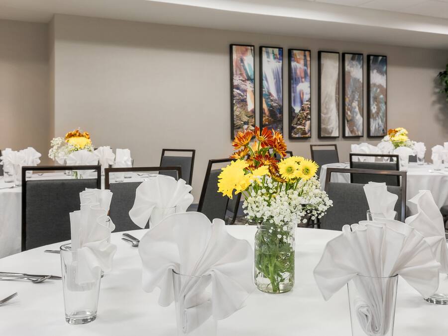 Une salle de conférence avec des tables rondes disposées pour les réunions, chacune agrémentée d’un centre de table en verre transparent et de serviettes blanches.