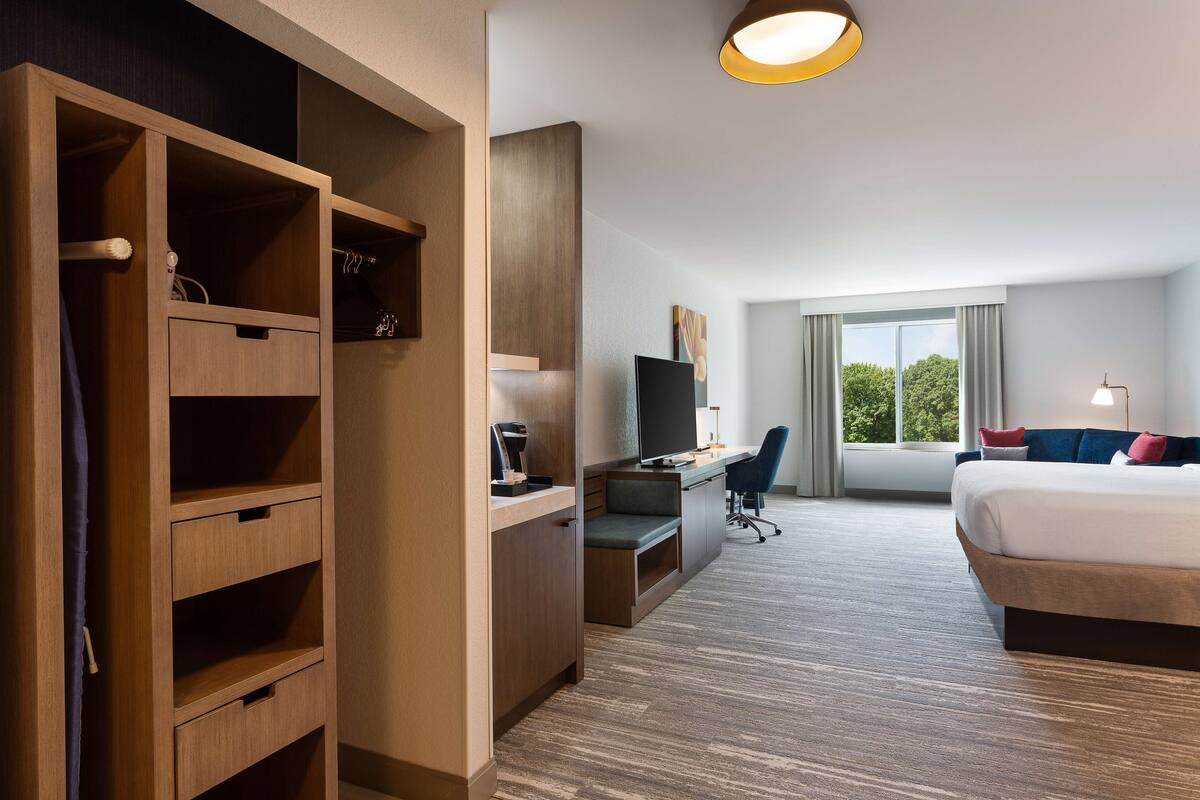 A hotel room with a bed, desk, TV, and a wardrobe.