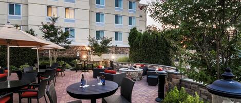 A hotel patio with outdoor seating, a stone wall, and a large building with a sign.
