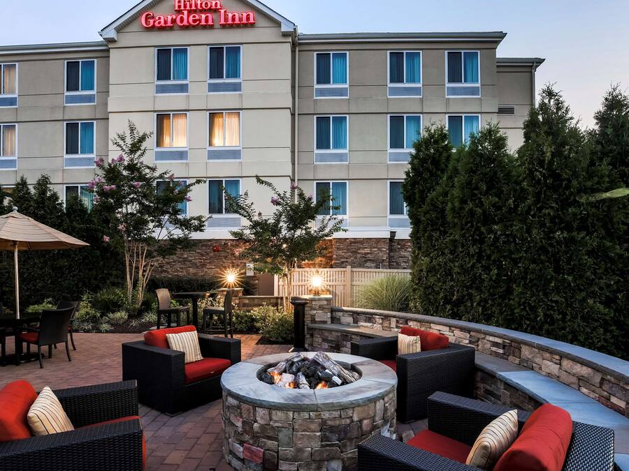 A hotel patio with outdoor seating, a stone fire pit, and a view of the hotel building.