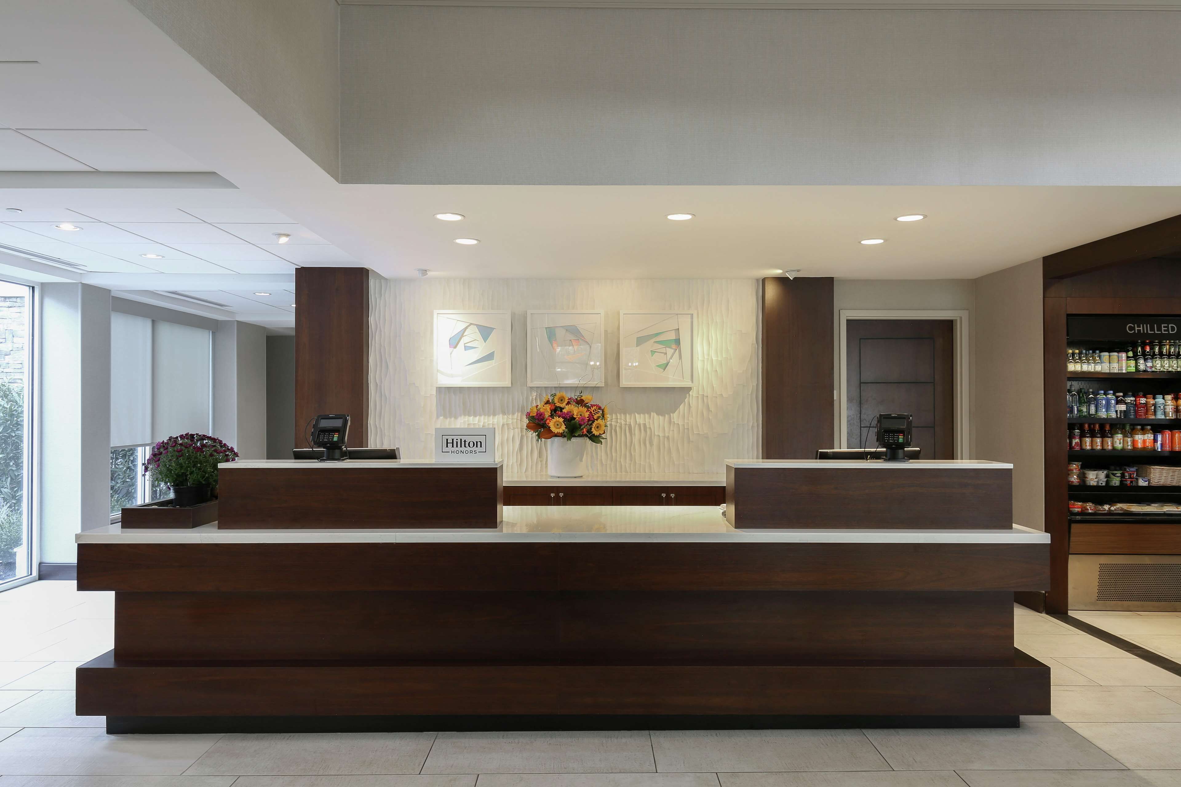 A modern reception desk with a wooden finish, a floral centerpiece, and a sign indicating it's a Hilton hotel.