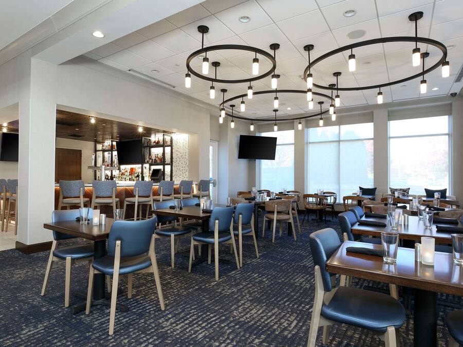 A hotel dining area with multiple tables and chairs, a bar area, and a large TV screen.