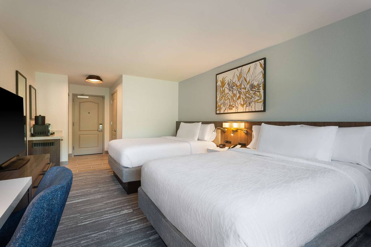A hotel room with two beds, a desk, a TV, and a painting on the wall.