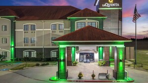 A hotel with a prominent entrance, a flag, and a sign with a sun logo. - La Quinta Inn & Suites by Wyndham Alvarado (Alvarado)