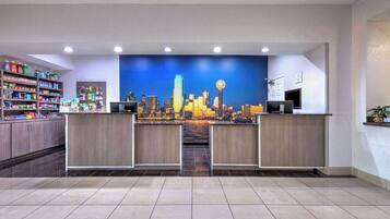 Zona de recepción de un hotel con un mural de la ciudad, un mostrador de recepción y una estantería con artículos de aseo.