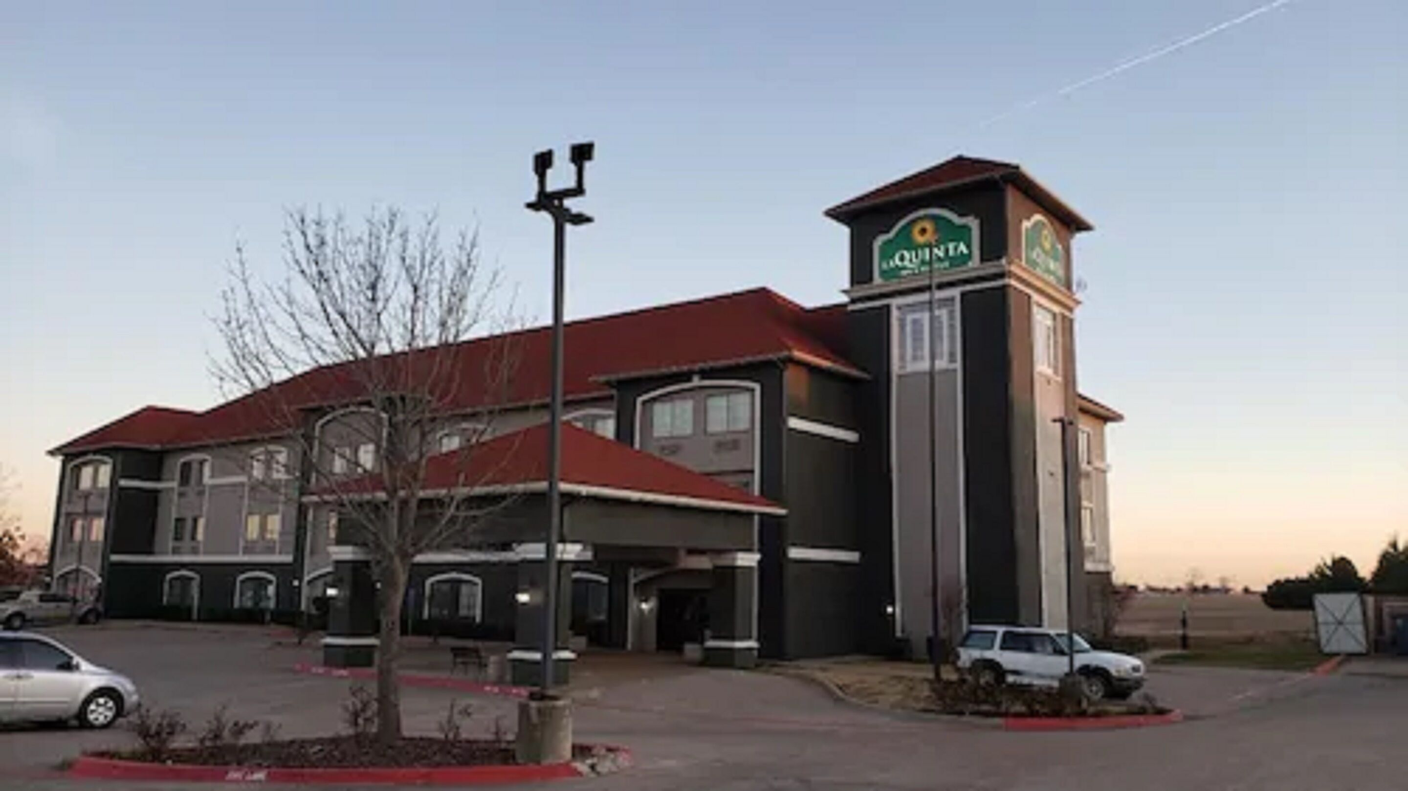 A hotel with a red roof, a tower with a sign, and a parking lot with cars.