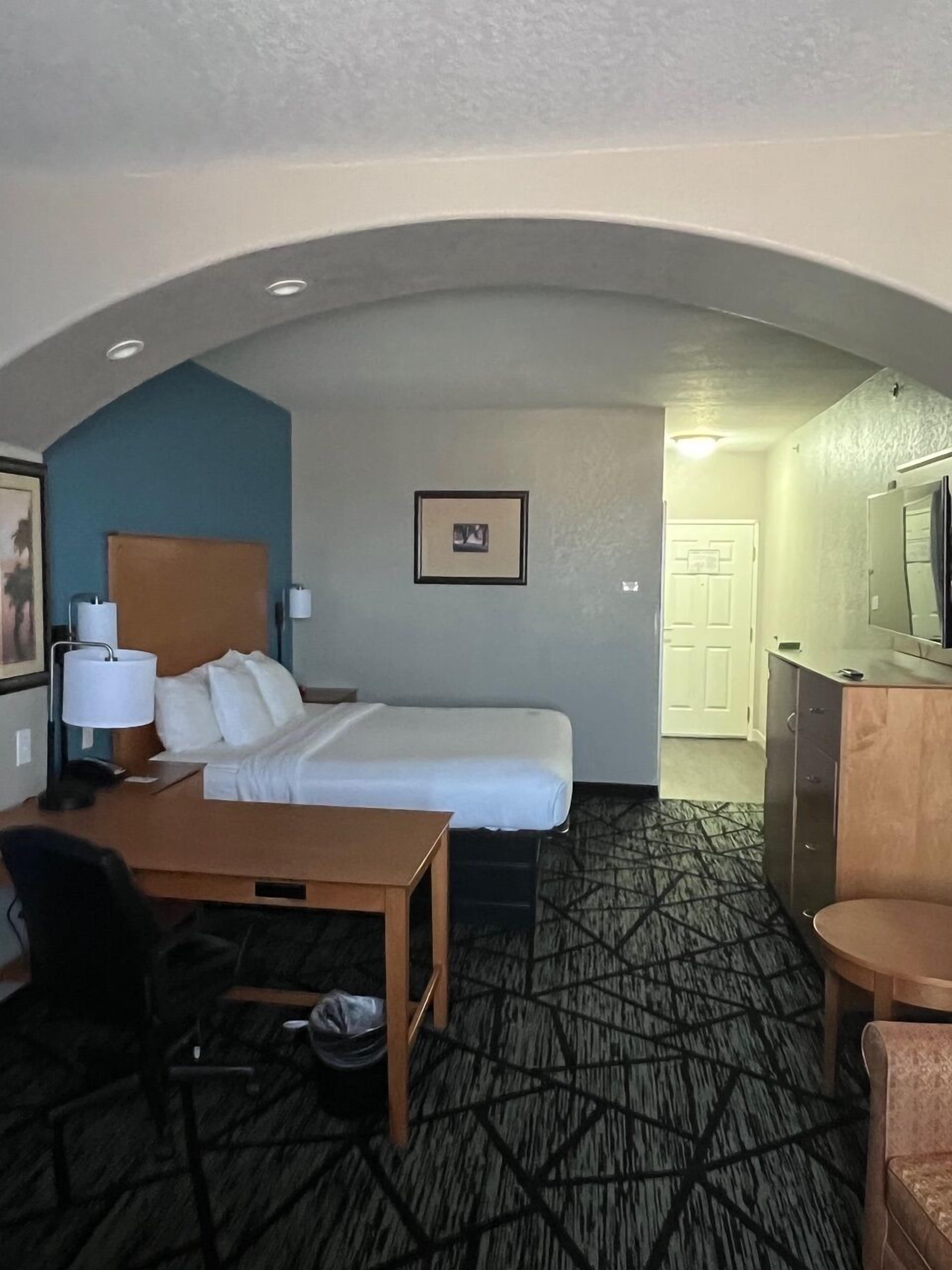 A hotel room with a bed, desk, chair, and a TV.