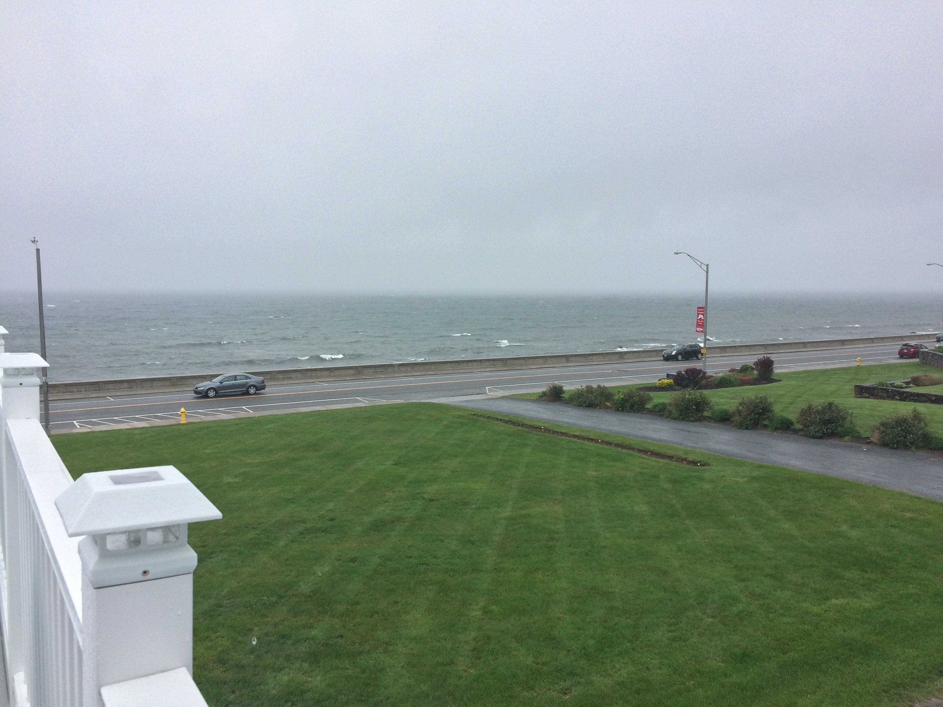 A coastal road with a grassy area in the foreground and the ocean in the background.