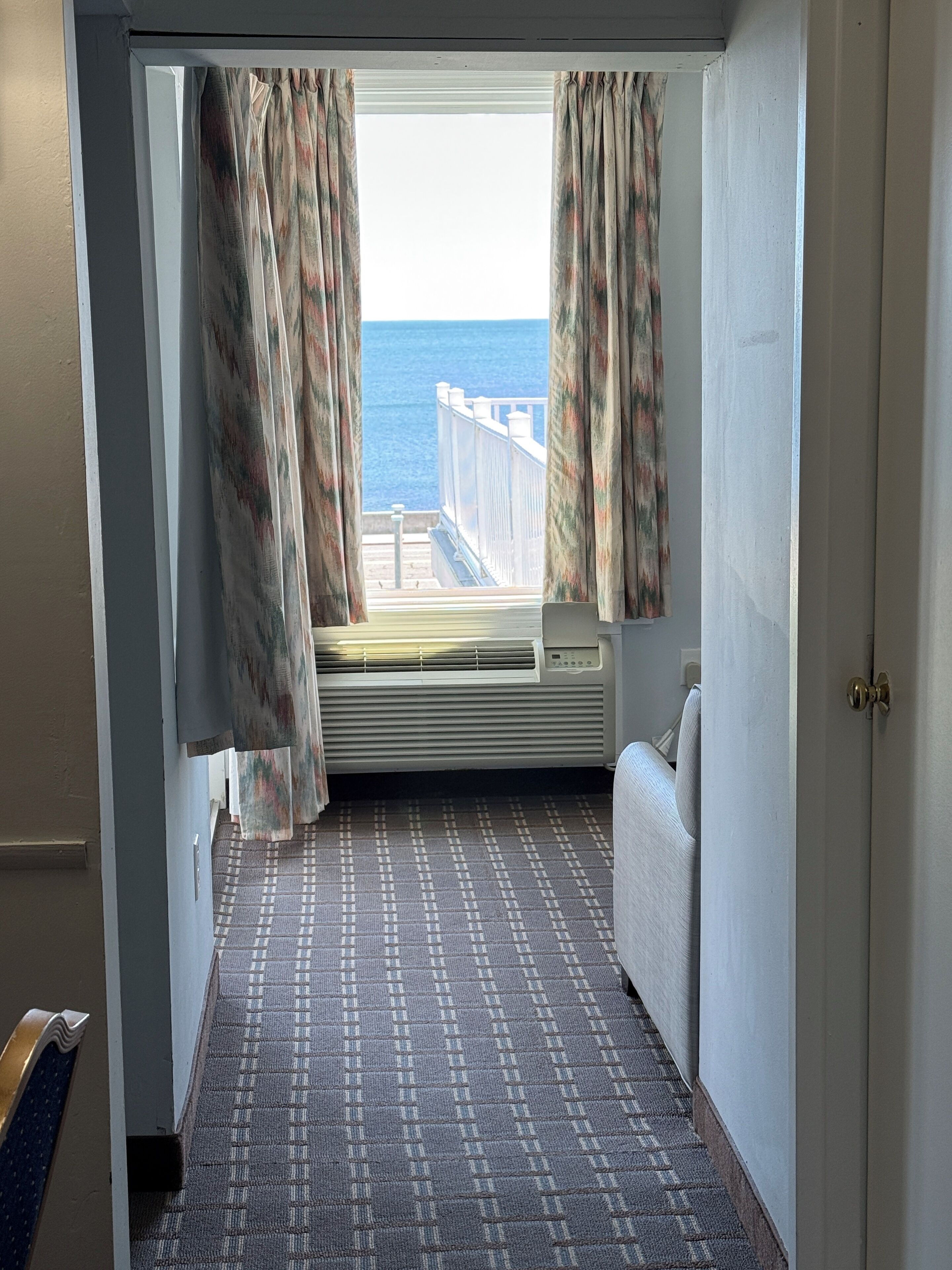A narrow hallway with a patterned carpet, a window with curtains, and a view of the sea.