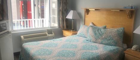 Hotellihuone, jossa on sänky, ikkuna verhoilla, lamppu, puinen pääty ja lämmitin.