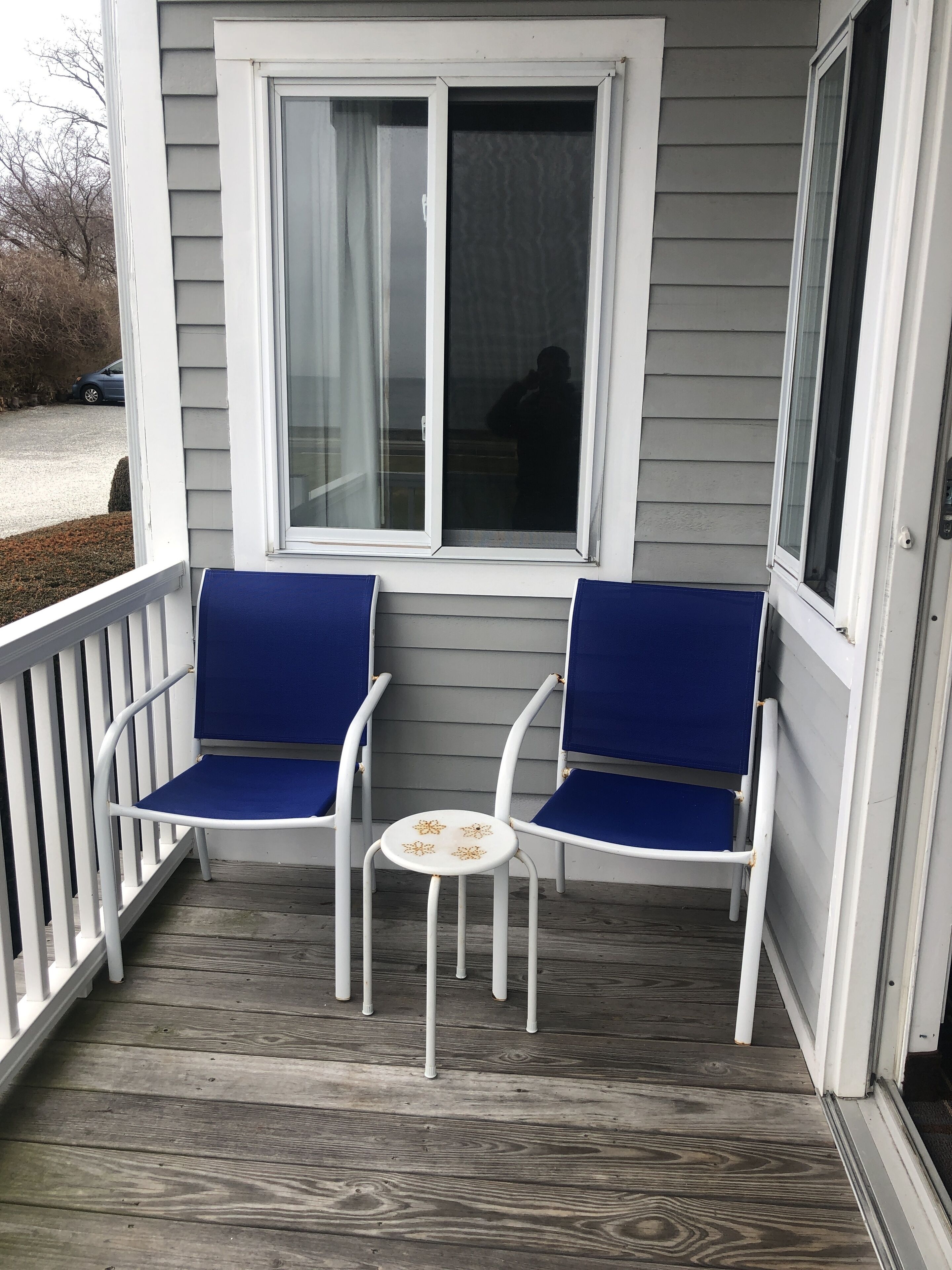 A porch with two white chairs and a small table, a window, and a railing.