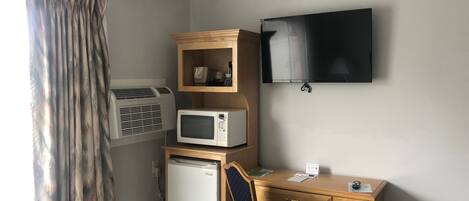 Una habitación compacta con escritorio, microondas, refrigerador, televisor y aire acondicionado.