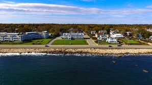 A coastal town with a prominent white building with a green lawn in front, situated next to a rocky shoreline. - Atlantic House (Narragansett)